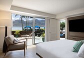 A hotel room with a large bed, a TV, a chair, and a view of the beach and ocean.