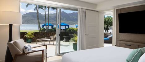 Habitación de hotel con una cama grande, televisión, una silla y vista a la playa y al océano.