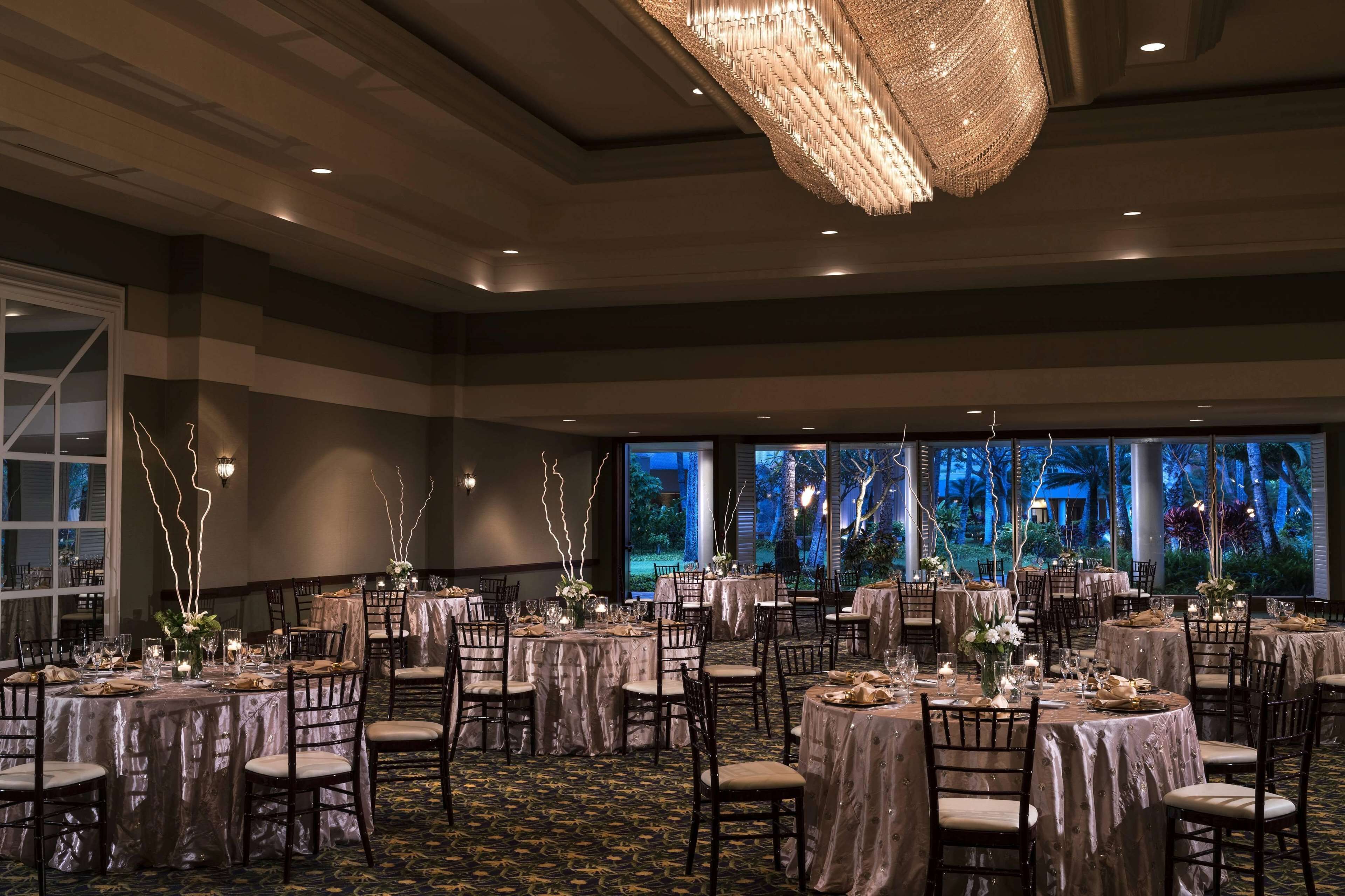 A banquet hall with round tables covered in tablecloths, chairs, and floral centerpieces.
