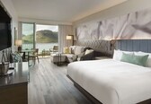 A hotel room with a large bed, a sofa, a dining table, and a view of the mountains.