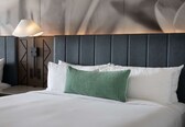 A neatly made bed with white linens and a green accent pillow, a modern lamp, and a geometric wall panel.