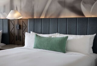 A neatly made bed with white linens and a green accent pillow, a modern lamp, and a geometric wall panel.