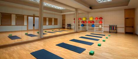 A spacious room with wooden flooring, large mirrors, and exercise mats.