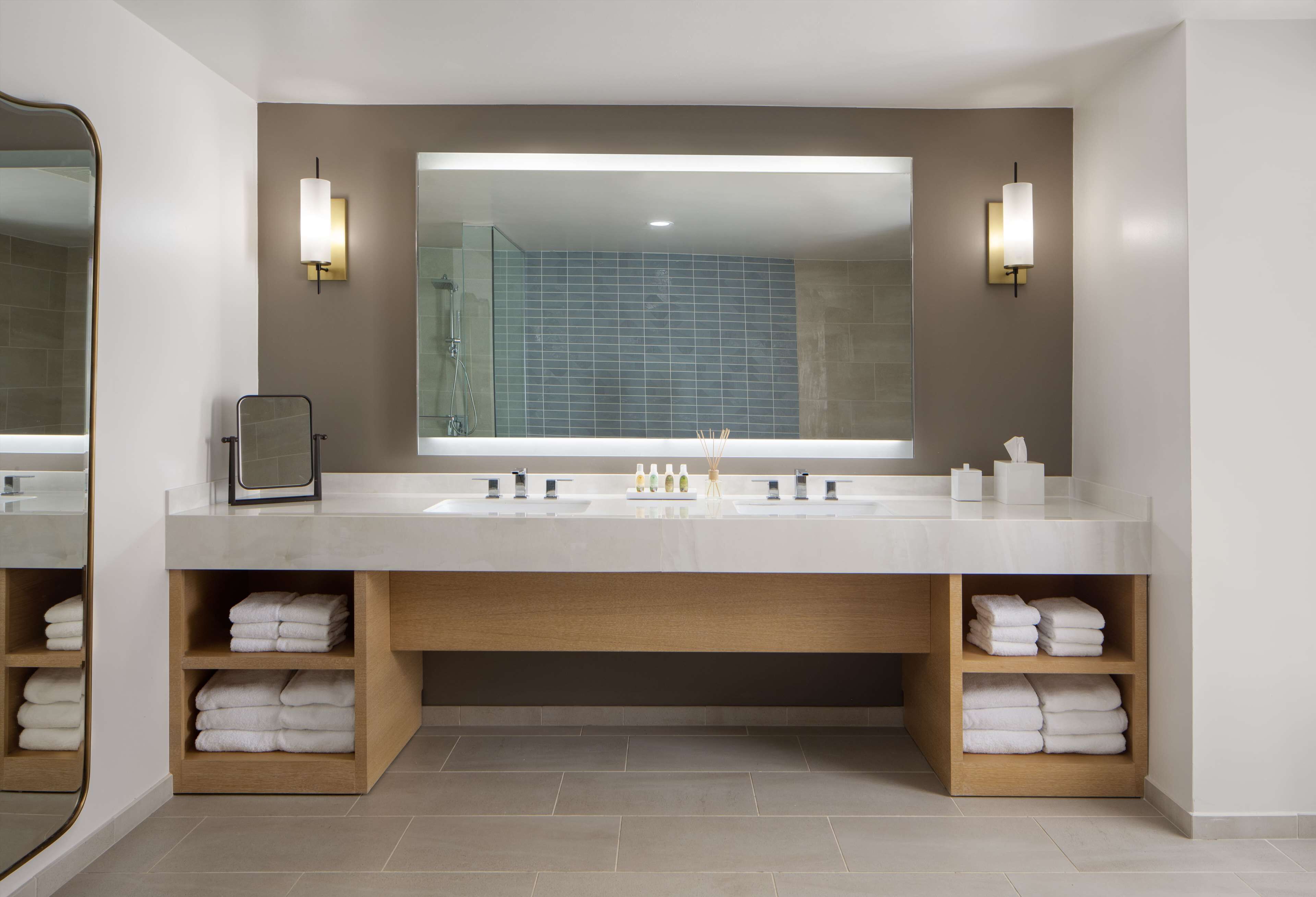 Une salle de bain moderne avec un grand miroir, deux lavabos et des étagères pour les serviettes.