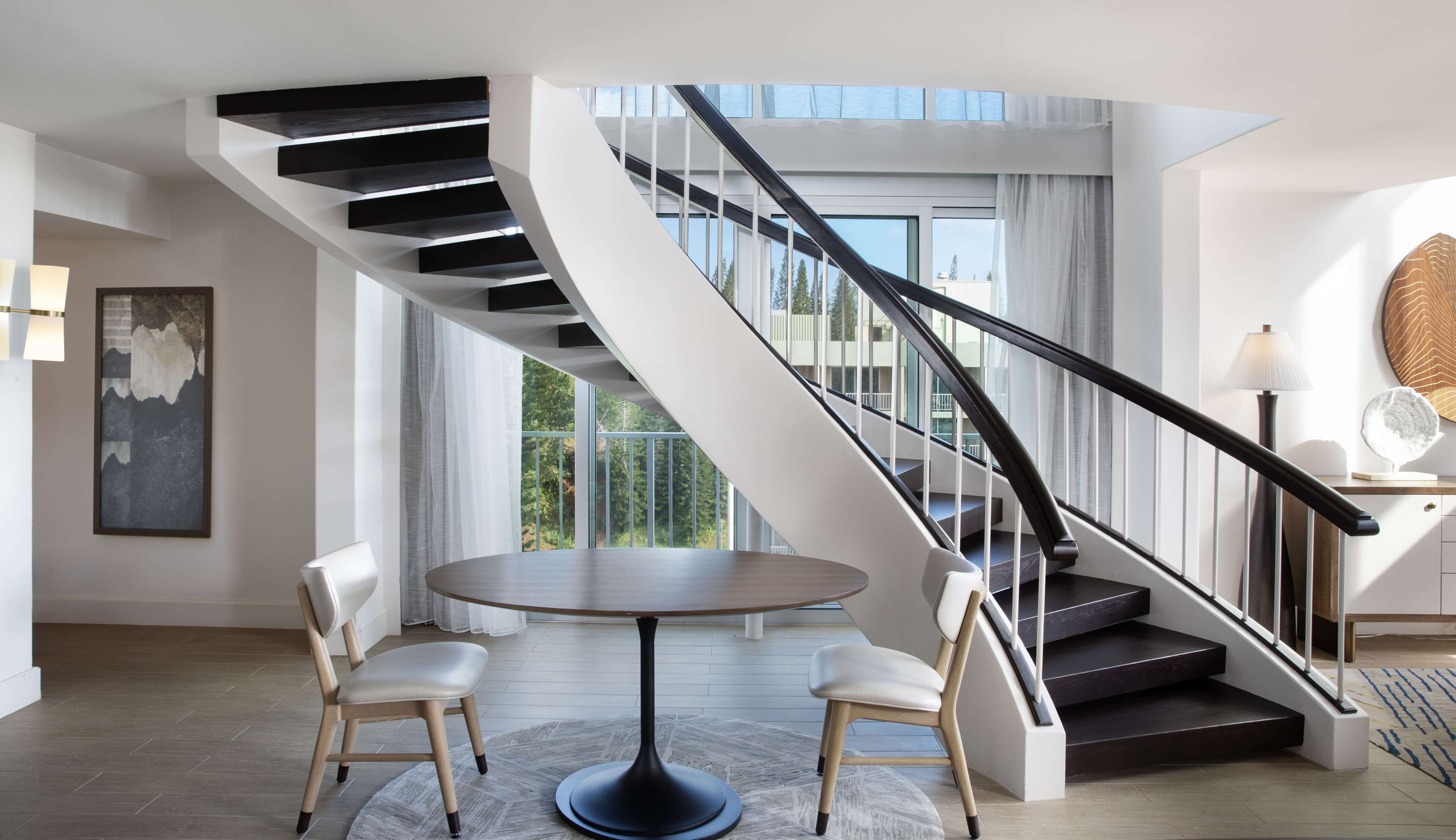 A modern interior with a spiral staircase, a round dining table, and two chairs.
