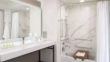 A modern bathroom with a large mirror, two sinks, a shower with a handheld showerhead, and a wooden shelf.