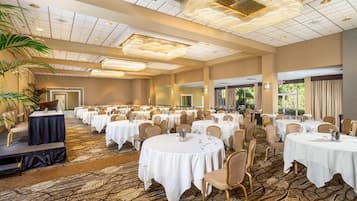 A large banquet hall with round tables, chairs, and a stage.