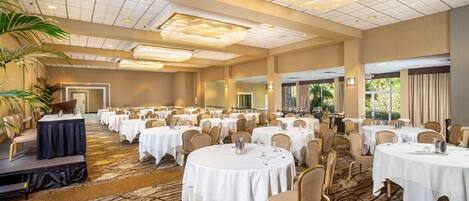 A large banquet hall with round tables, chairs, and a stage.