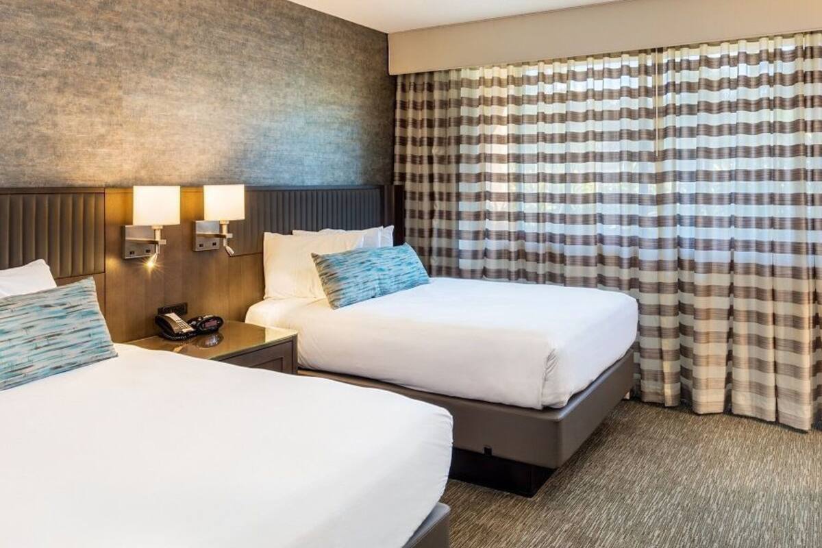A hotel room with two beds, a headboard, bedside lamps, a telephone, and a window with curtains.