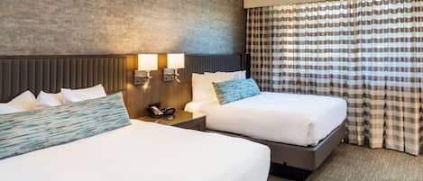 Habitación de hotel con dos camas, cabeceros, lámparas de noche, teléfono y una ventana con cortinas.