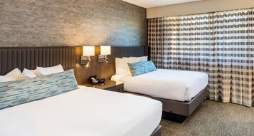 A hotel room with two beds, a headboard, bedside lamps, a telephone, and a window with curtains.