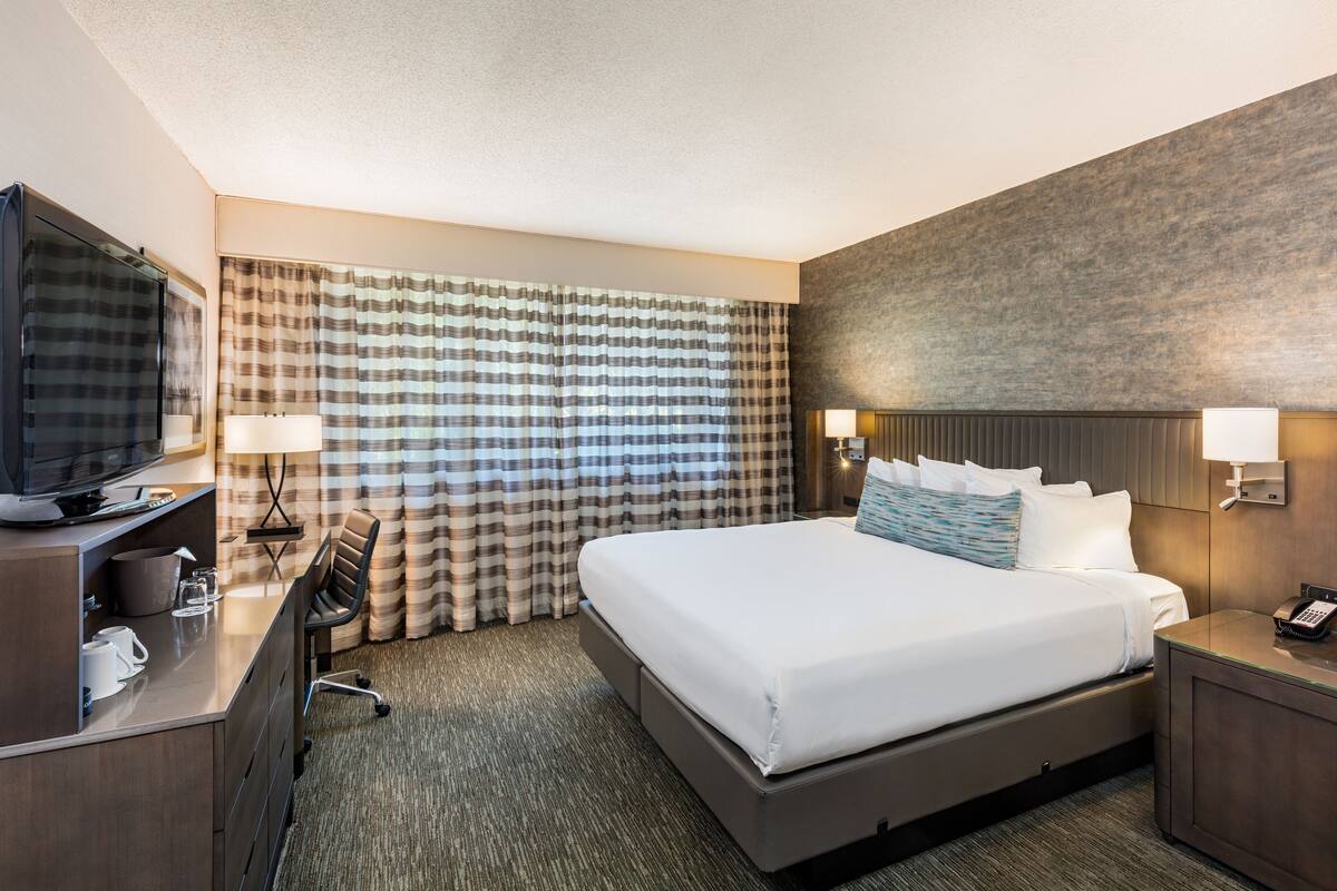 A hotel room with a large bed, a desk with a television, a lamp, and a telephone.