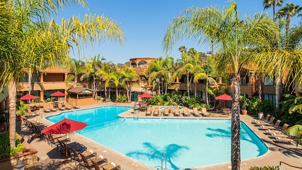 Un resort con una piscina grande rodeada de sillones de descanso y palmeras.