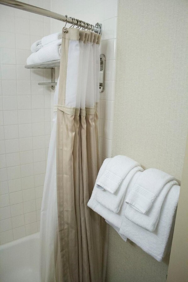 A bathroom with a shower curtain, a towel rack with folded towels, and a bathtub.