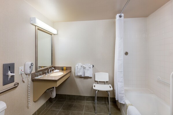 A bathroom with a sink, mirror, towel rack, shower, and a wheelchair-accessible chair.