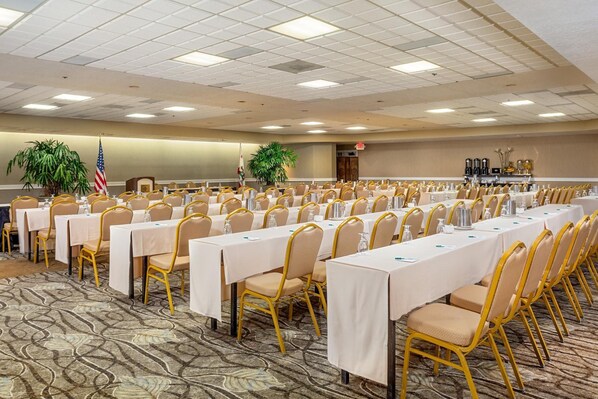 A conference room with rows of tables and chairs, flags, and a carpeted floor.