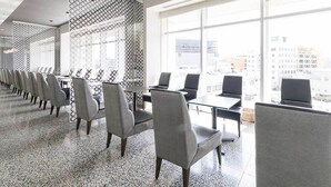 A modern conference room with rows of grey chairs and tables, large windows offering a city view, and a patterned wall divider. - Naha Tokyu REI Hotel (Naha)