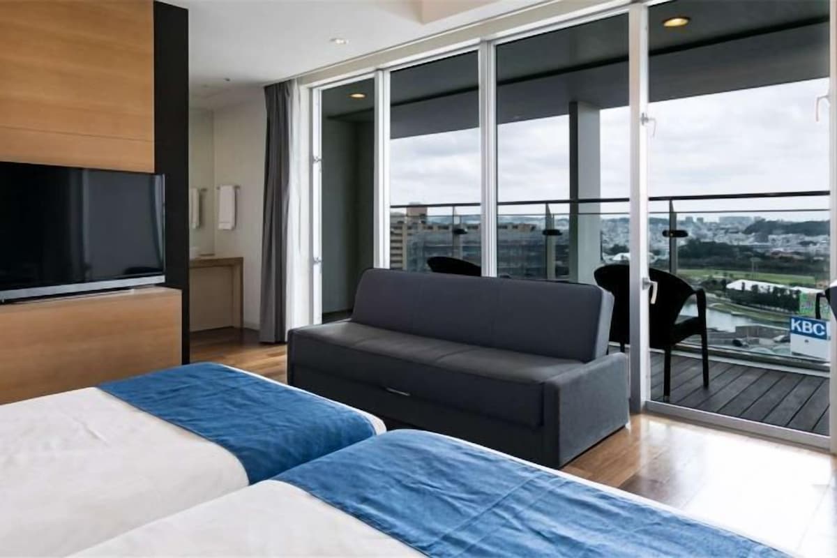 A modern hotel room with a balcony, a bed, a sofa, and a TV.