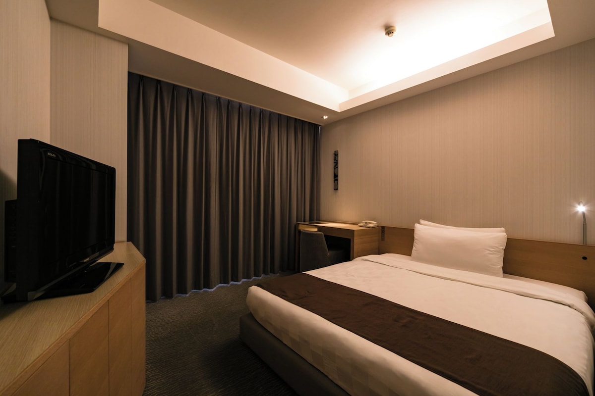 A hotel room with a bed, a desk, a television, and a curtain.