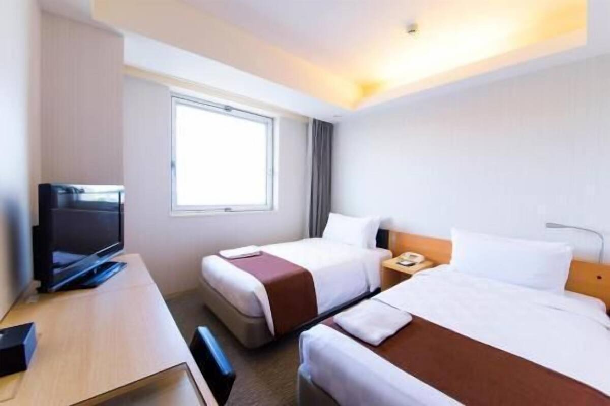 A hotel room with two beds, a TV, a desk, and a window.