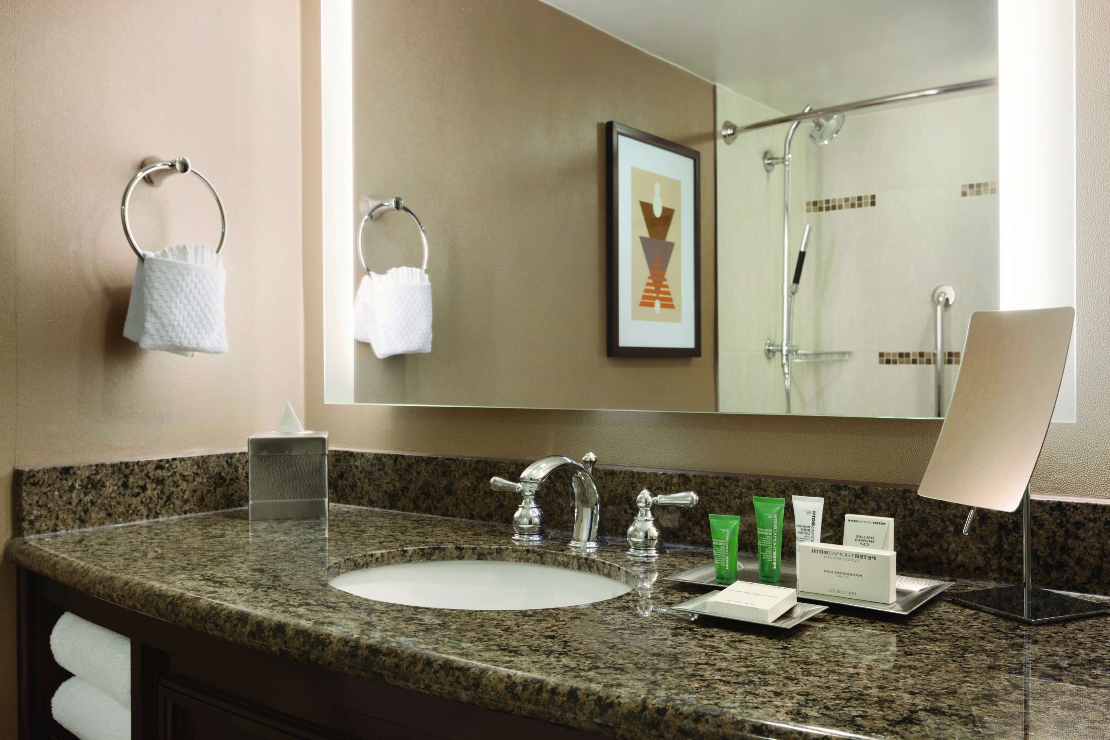Une salle de bain avec un comptoir en granit, un lavabo, un miroir et un tableau encadré au mur.
