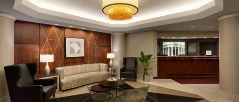 A modern lobby with a reception desk, a sofa, two armchairs, a coffee table, and a chandelier.