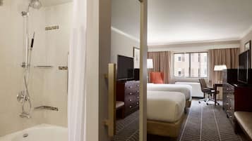 Una habitación de hotel con bañera, dos camas, un escritorio y un televisor.