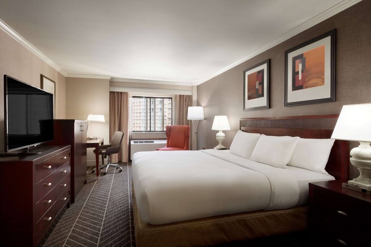 A hotel room with a large bed, a desk, a television, and two lamps.