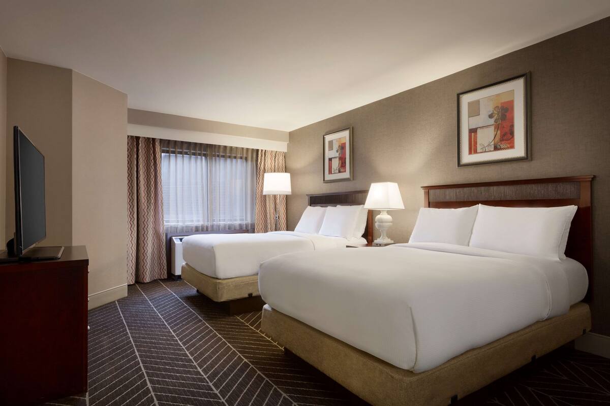 A hotel room with two beds, a TV, and a desk.