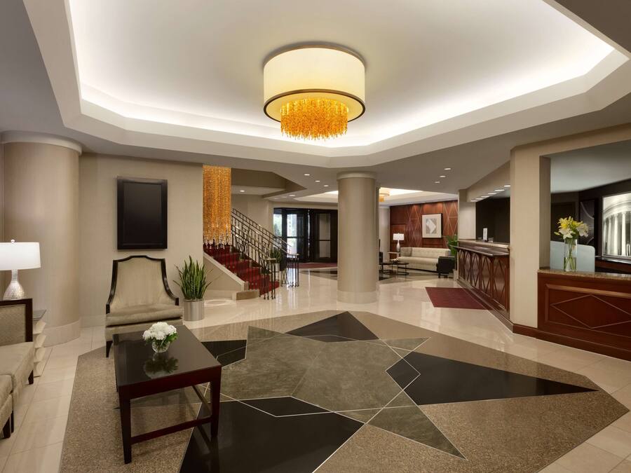 A modern hotel lobby with a central staircase, a reception desk, and a seating area with a coffee table and sofa.