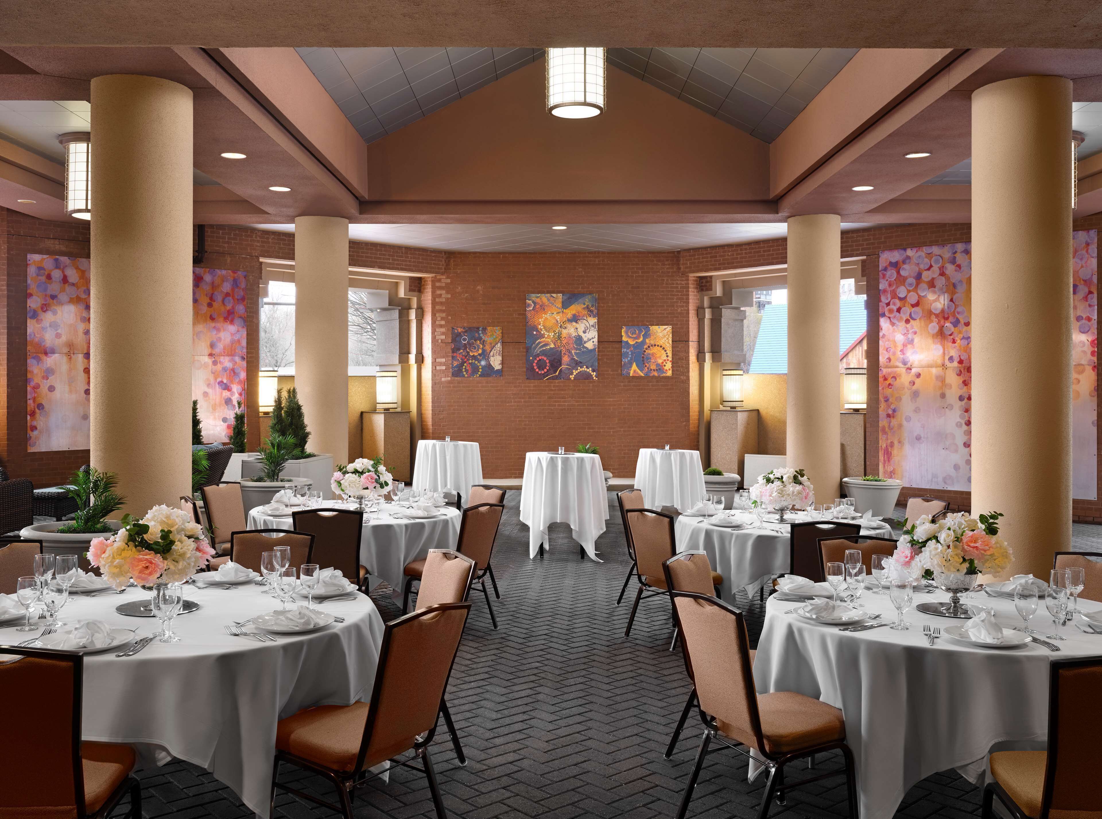 Un vaste espace intérieur aménagé en salle à manger, avec des tables rondes, des chaises et des œuvres d’art accrochées aux murs.