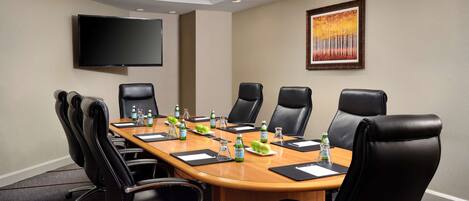 A conference room with a long table, black leather chairs, a flat-screen TV, and a framed painting on the wall.