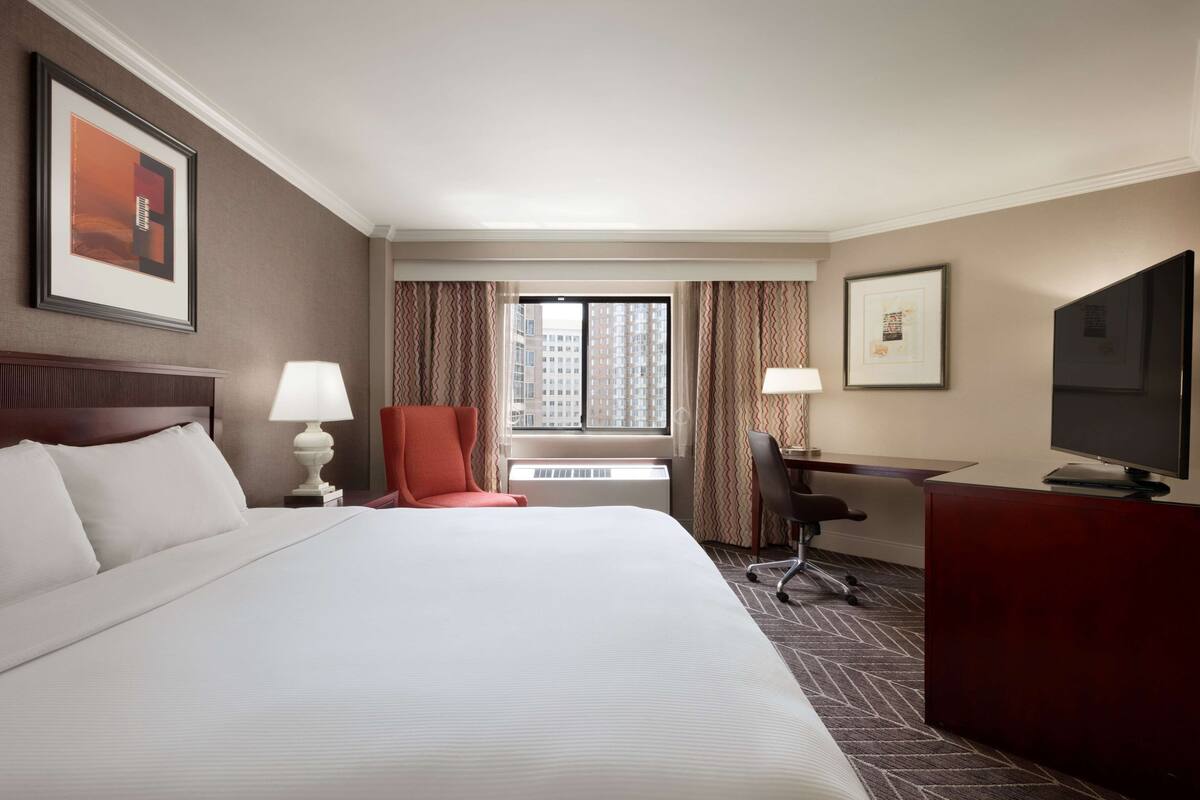 A hotel room with a large bed, a desk, a chair, a television, and a window with curtains.
