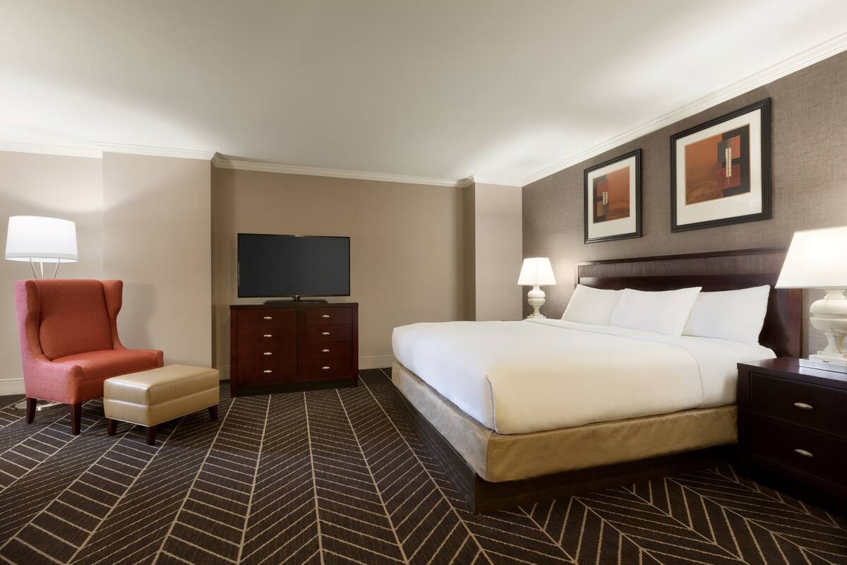 A hotel room with a large bed, a desk, a chair, a TV, and two framed pictures on the wall.