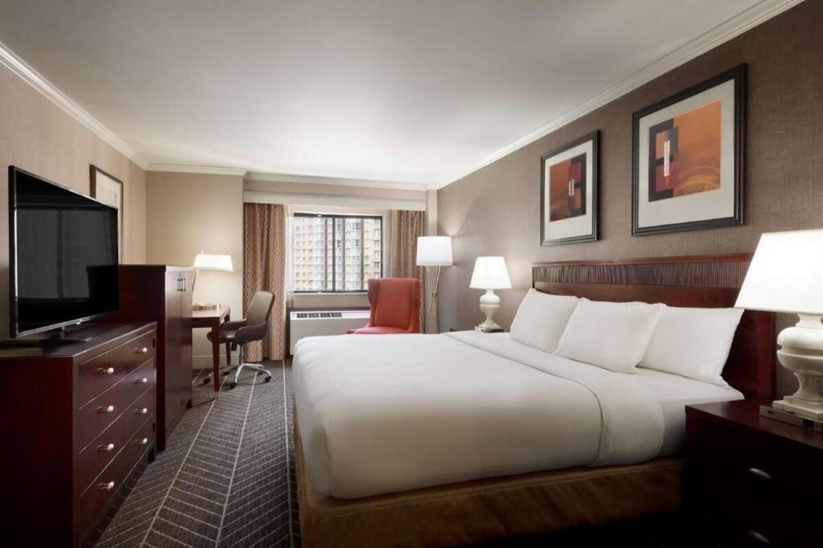 A hotel room with a bed, a desk, a chair, a television, and two lamps.