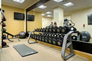 Une salle de sport équipée de matériel d’exercice, notamment des haltères, un tapis de course et un vélo d’appartement.