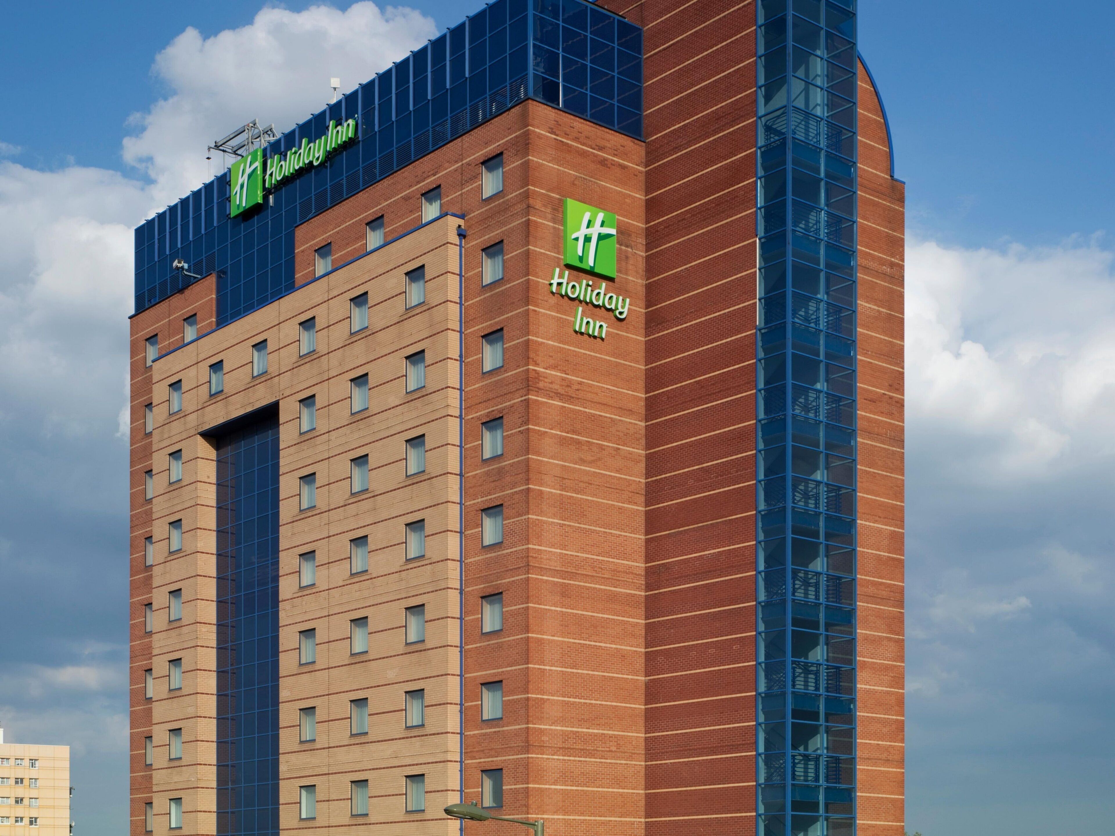 A Holiday Inn hotel building with a modern design, featuring a prominent logo and a clear sky in the background.