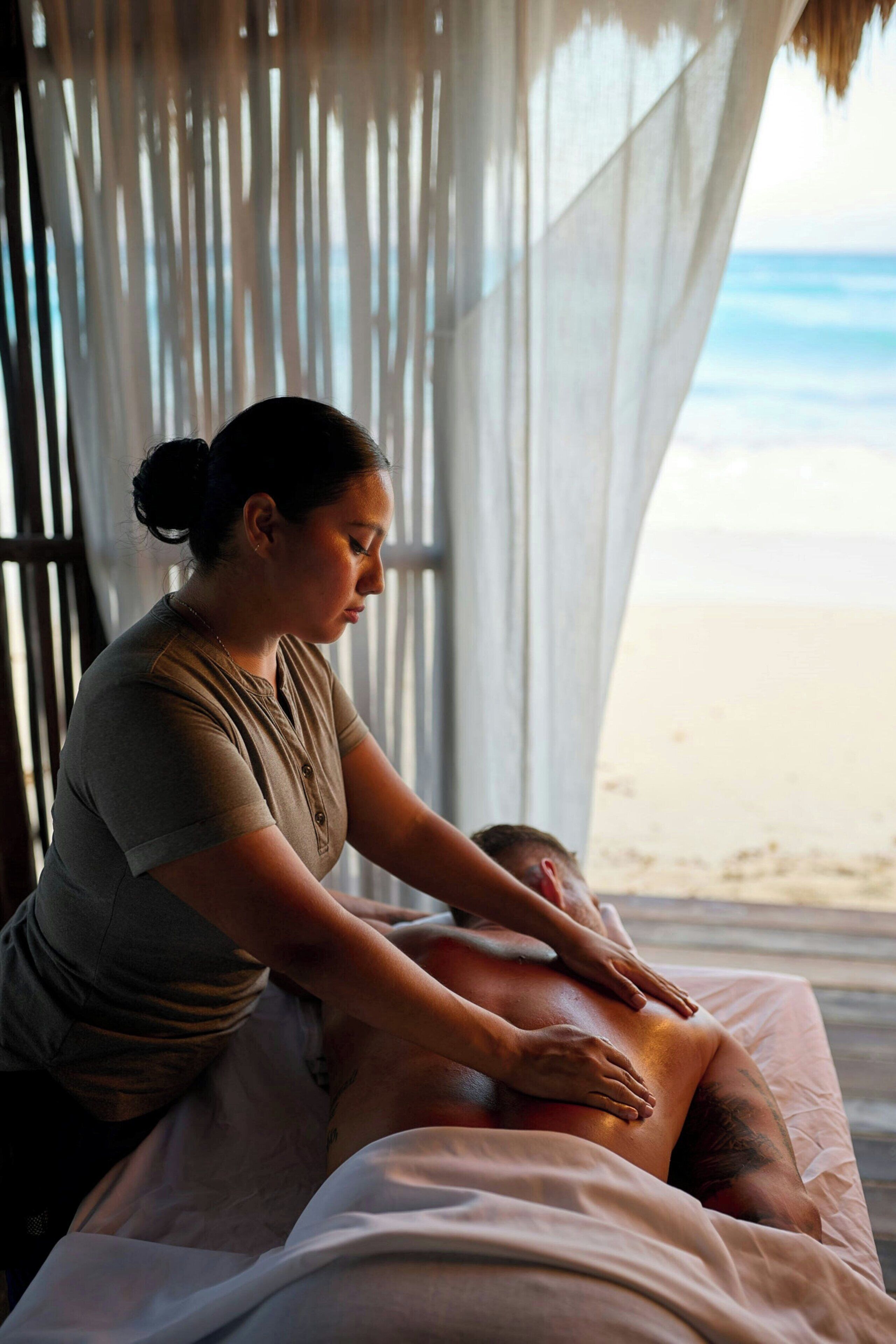 Iemand ontvangt een massage op een bed, met uitzicht op het strand.