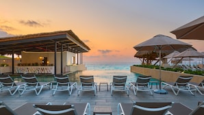 A poolside area with lounge chairs and umbrellas, overlooking a body of water during sunset. - Marriott Cancun  Resort (Cancun)