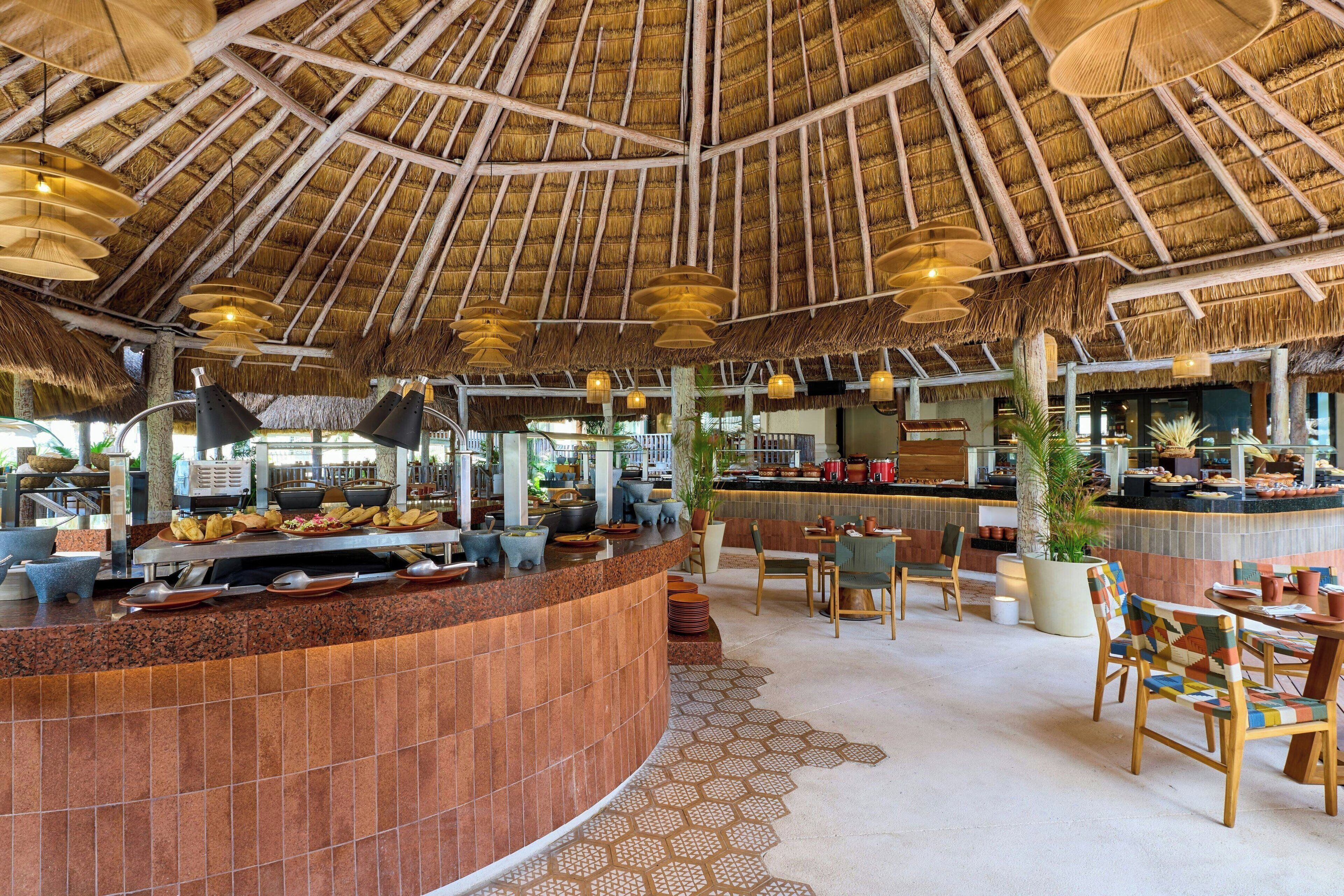 Een restaurant met rieten dak, een buffet en houten stoelen en tafels.
