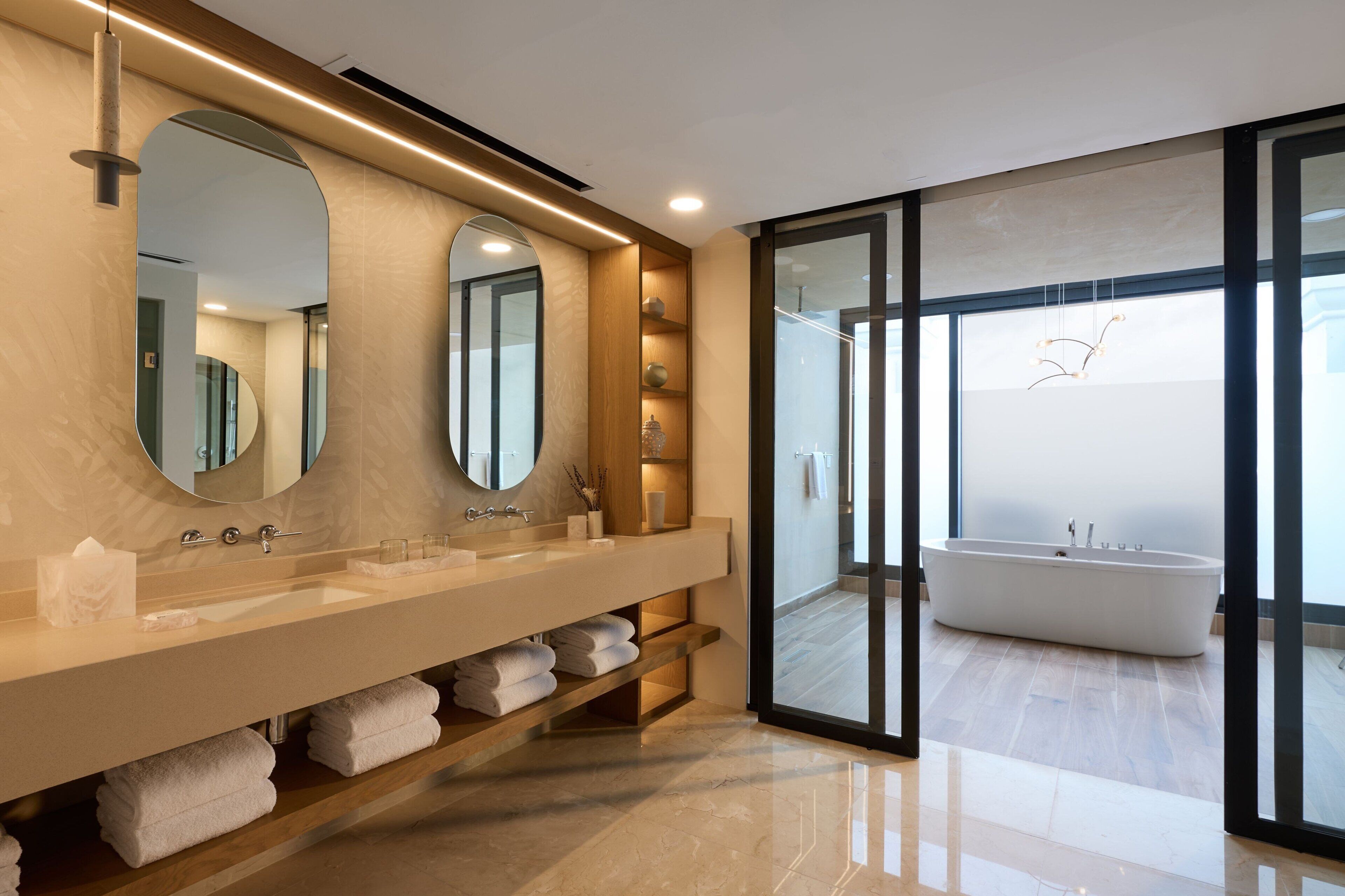 A modern bathroom with a large vanity, two mirrors, a bathtub, and a glass shower enclosure.