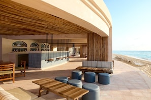 Un área de descanso en la playa con mobiliario de madera, una barra y vistas al océano.