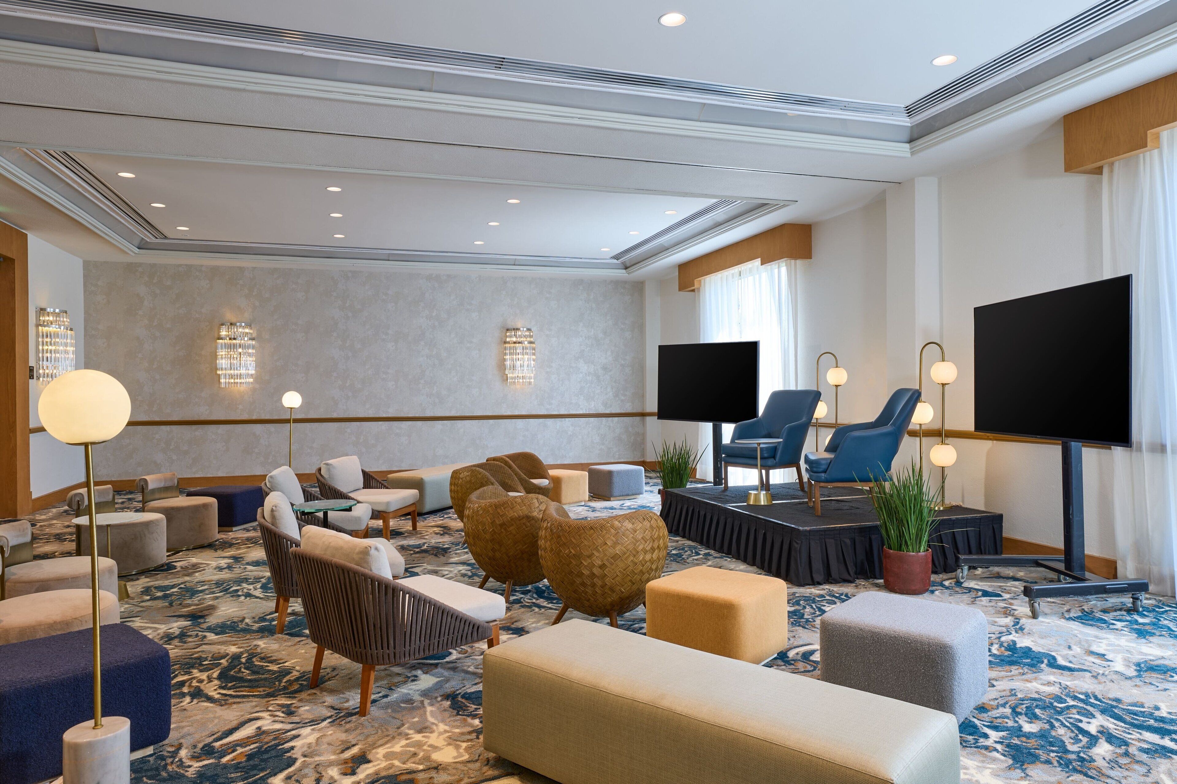 Un hall d’hôtel doté d’un tapis à motifs de marbre, de plusieurs espaces de détente comprenant des canapés et des fauteuils, d’un téléviseur à écran plat et d’appliques murales.