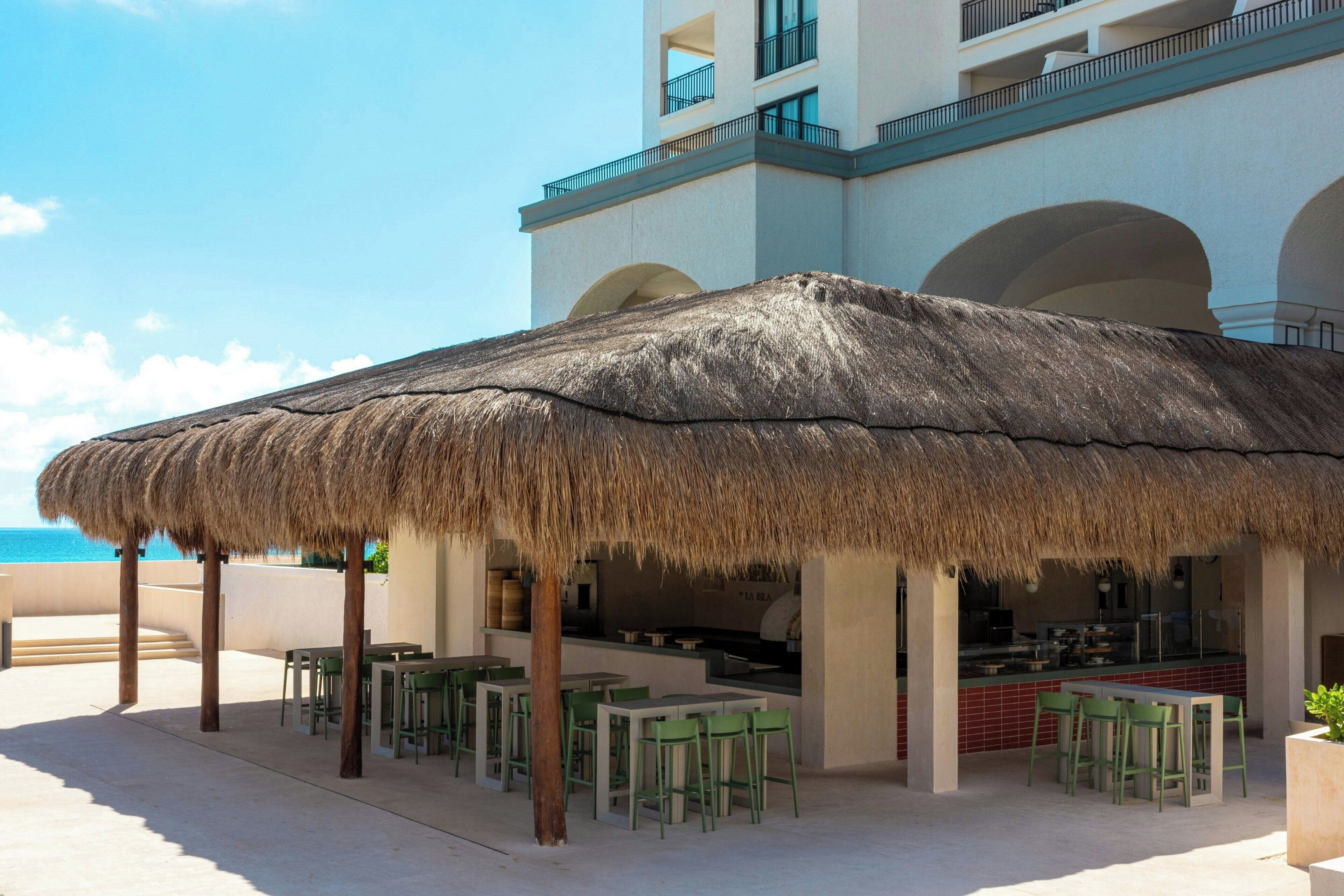 An outdoor dining area with a thatched roof, green chairs, and a view of the ocean.
