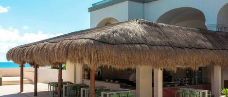 An outdoor dining area with a thatched roof, green chairs, and a view of the ocean.