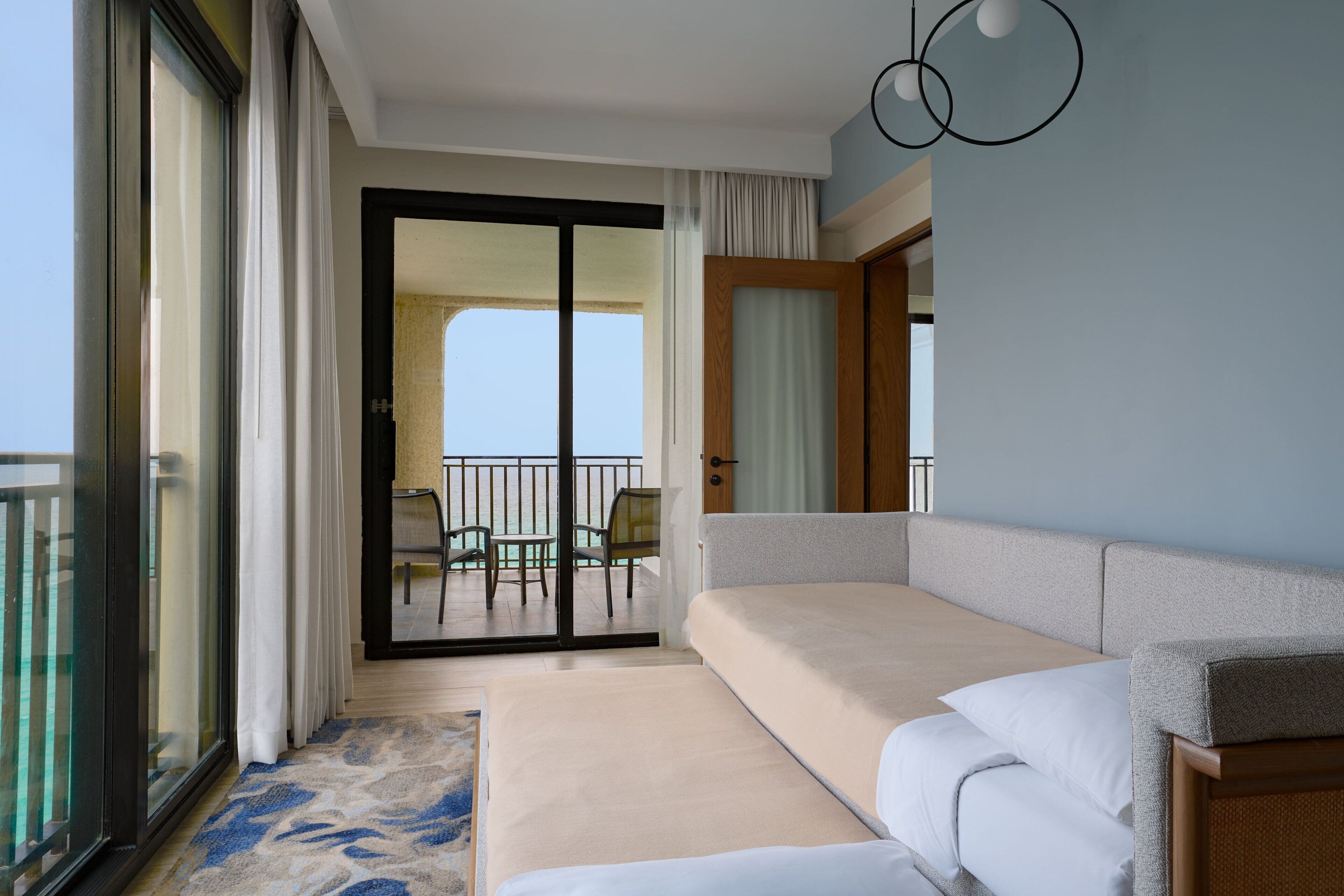 A hotel room with a large bed, a balcony with a view, and a sliding glass door leading to an outdoor seating area.