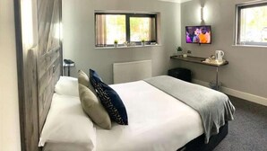 A hotel room with a bed, a TV, a small table, and a window with curtains. - Fairways Lodge & Leisure Club (Manchester)