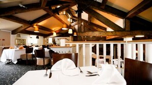 A restaurant with wooden beams, white tables, and chairs. - Fairways Lodge & Leisure Club (Manchester)