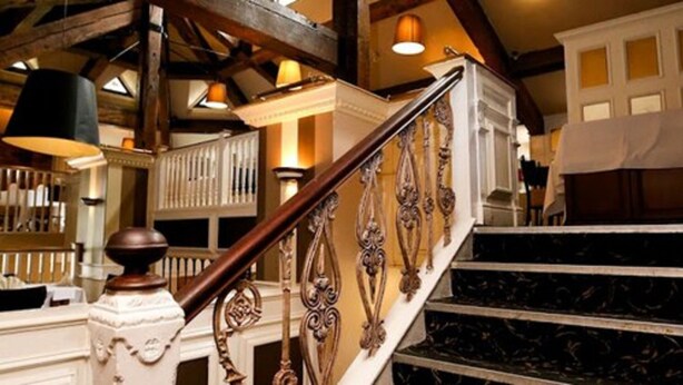 A staircase with ornate balusters and a wooden handrail, leading to a landing with a white railing and a view of the interior. - Fairways Lodge & Leisure Club (Manchester)