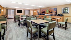A hotel dining area with multiple tables and chairs, a kitchen counter with appliances, and a television mounted on the wall. - La Quinta Inn & Suites by Wyndham Irvine Spectrum (Irvine)